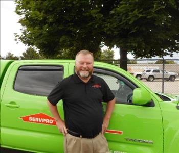 a man in a black shirt standing in front of a green SERVPRO truck