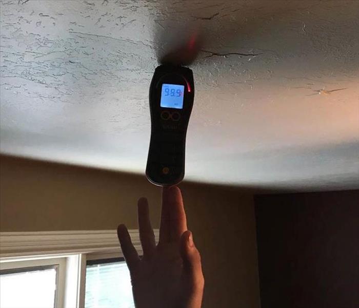 Man holds moisture meter up to a ceiling after water damage